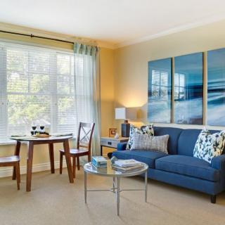 A bright and cozy living room with a blue sofa, modern artwork, and a small dining area by the window.