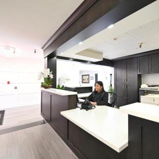 A modern office reception area with a dark wooden desk and a person working at the counter.