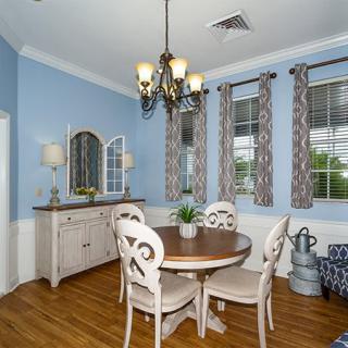 A cozy dining room with blue walls, featuring a round wooden table and four chairs under a chandelier.