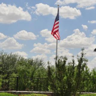 An American flag waving under a bright, cloudy sky with trees in the background.