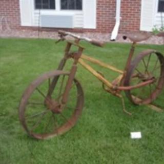 A rusty vintage bicycle sculpture displayed on a grassy lawn.