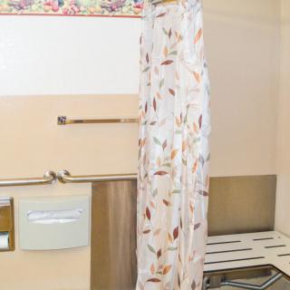 A bathroom featuring a floral shower curtain and handrails.