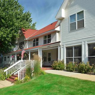 A two-story residential house with a red roof, white siding, and a well-maintained lawn.
