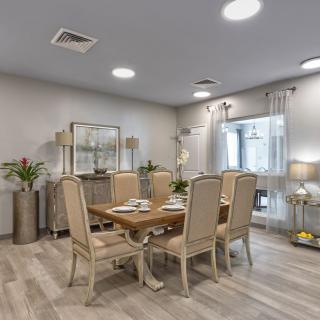 A modern dining room with a wooden table and elegant chairs, decorated in neutral tones with stylish lighting and greenery.