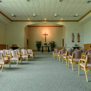An interior view of a chapel with rows of chairs and a cross at the front.