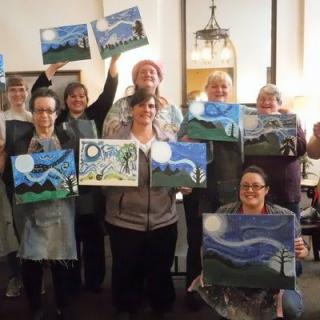 A group of adults proudly displaying their landscape paintings during an art class.