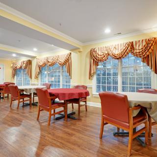 A well-lit dining room with neatly arranged tables and chairs, adorned with decorative curtains and large windows.