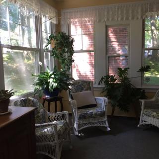 A cozy sunroom with wicker furniture and lush green plants, bathed in natural light.