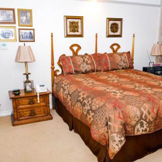 A cozy bedroom with a patterned bedspread, matching lamps, nightstands, and framed artwork on the wall.