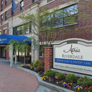 Entrance to a building with a blue awning and adjacent signage for a senior living community.