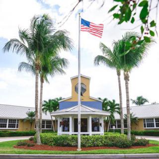 A building with an American flag flying in front, surrounded by palm trees.