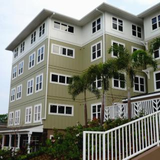 A four-story residential building with a green facade and white-trimmed windows, surrounded by palm trees.