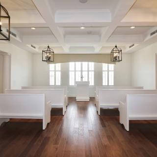 A serene chapel interior featuring white pews and wooden flooring.