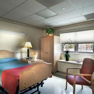 A clean and well-organized hospital room with a single bed, chair, and window.