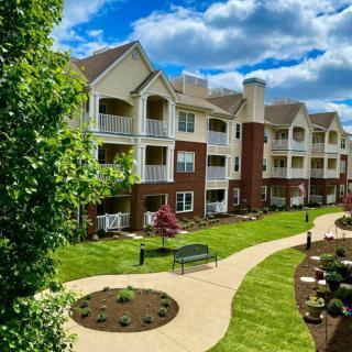 A well-maintained apartment complex with lush landscaping and walking paths under a partly cloudy sky.
