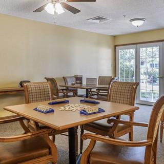 A cozy game room with a table set up for playing dominoes, featuring comfortable chairs and natural light from a large window.