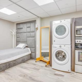 A modern room combining laundry and bedroom features with stacked washer and dryer, single bed, and contemporary decor.