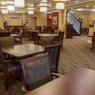 A well-lit dining area with multiple tables and chairs, featuring a carpeted floor and formal ambiance.