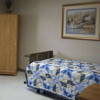 A simple bedroom with a single bed adorned with a patchwork quilt, a wooden wardrobe, and a painting on the wall.
