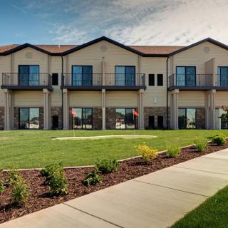A modern two-story building with large windows, surrounded by a neatly landscaped lawn and paved pathway.
