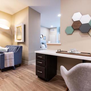 A modern living area featuring a cozy chair, wooden floors, and a stylish desk with geometric wall decor.