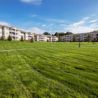 A spacious apartment complex with a large grassy area in the foreground under a clear blue sky.