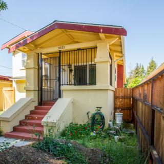 A small residential house with a front porch and a fenced yard.