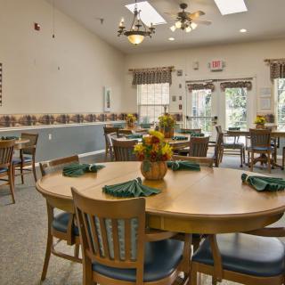 A well-lit dining room with neatly arranged tables and chairs, featuring floral centerpieces for decoration.