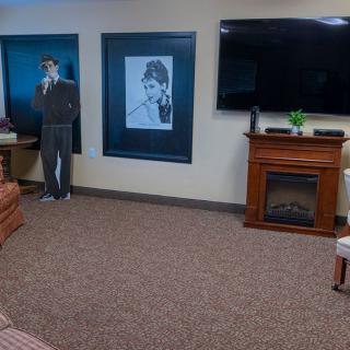 A cozy living room with a television, fireplace, artwork on the wall, and a cardboard cutout.