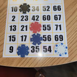 A bingo card on a table with some numbers covered by chips.