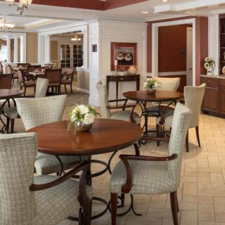 A cozy dining area with round tables and upholstered chairs, decorated with small flower arrangements.
