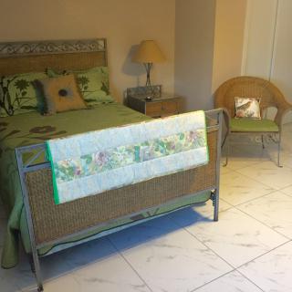 A cozy bedroom featuring a metal bed with green accents, a wicker chair, and a bedside lamp.
