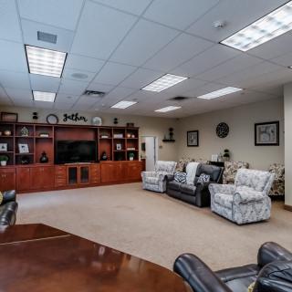 A spacious conference room featuring comfortable seating, a large shelving unit, and ample lighting.