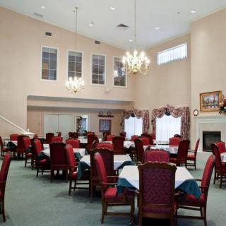 A spacious dining room interior with arranged tables and chairs, chandeliers overhead, and large windows adorned with curtains.