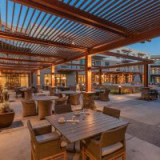 An inviting outdoor restaurant patio under a pergola, warmly lit in the evening.