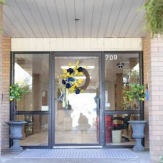 A building entrance with glass doors adorned by a decorative wreath and flanked by potted plants.