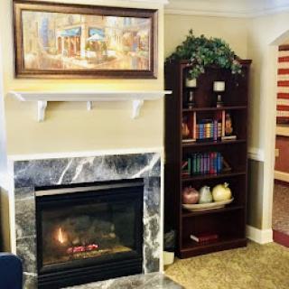 A cozy living room setup featuring a marble fireplace, a bookshelf filled with books, and a piece of artwork above the mantel.