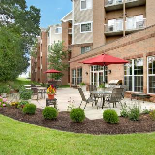 A well-maintained outdoor patio area with tables, chairs, and red umbrellas in front of an apartment building.