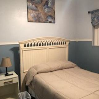 A cozy bedroom with a neatly made bed, accented by a nightstand and lamp, featuring a soft color palette and wall art.
