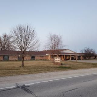 A view of a residential building with trees and grass in the foreground, located alongside a road.