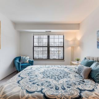 A cozy bedroom with a large window, featuring a stylish bedspread and a comfortable chair.