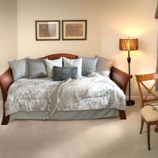 A cozy bedroom featuring a daybed with pillows, a floor lamp, and a wooden chair.