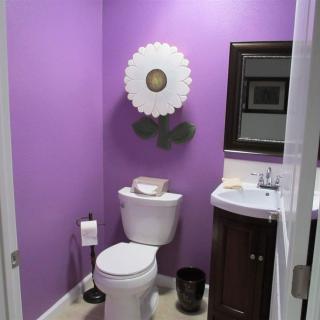A bathroom with purple walls featuring a toilet, sink, mirror, and decorative wall art.