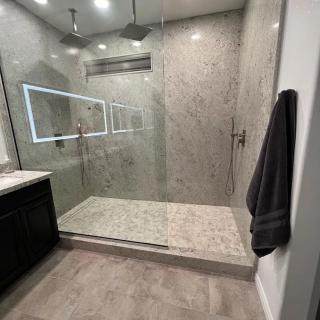 A modern bathroom featuring a spacious glass-enclosed shower with elegant tile walls and a lighted mirror.