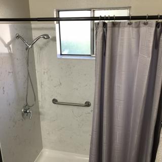 A shower area with a curtain, window, and grab bar.