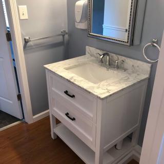 A bathroom with a white vanity and marble countertop, featuring a sink and mirror.