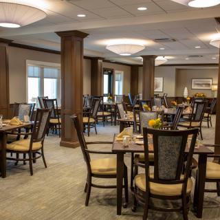 An elegant dining area with neatly arranged tables and chairs, featuring warm lighting and wooden accents.