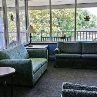 A cozy living room with sofas, a lamp, and large windows overlooking a green view.