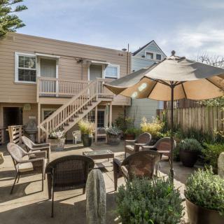 A cozy backyard patio with ample seating, surrounded by lush plants and shaded by an umbrella.
