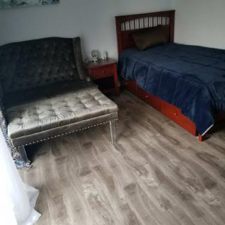 A cozy bedroom featuring a bed and a comfortable chaise lounge with wooden flooring.
